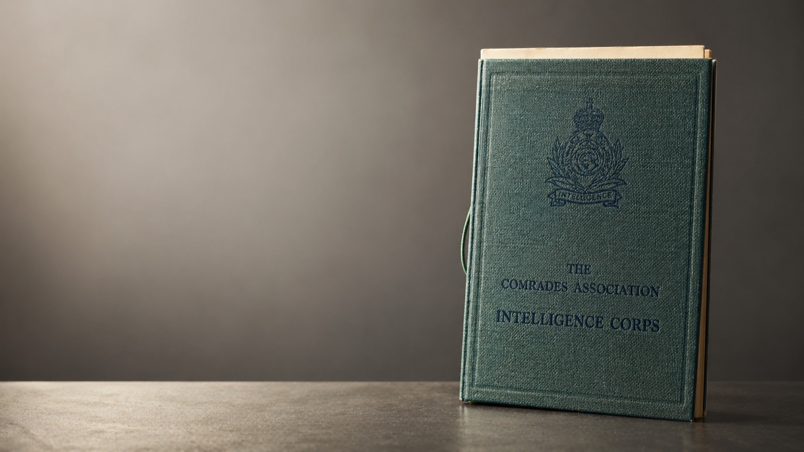 A vintage linen-bound copy of The Comrades Association Intelligence Corps handbook, embossed with the Corps cap badge